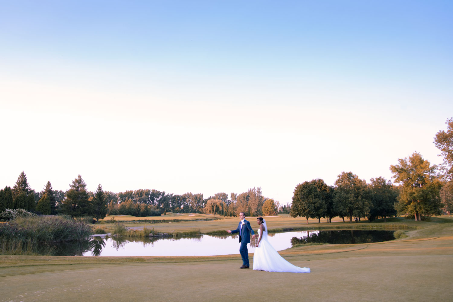 A candid panoramic wedding portrait of a multicultural couple walking across a golf course in Montreal, Quebec.